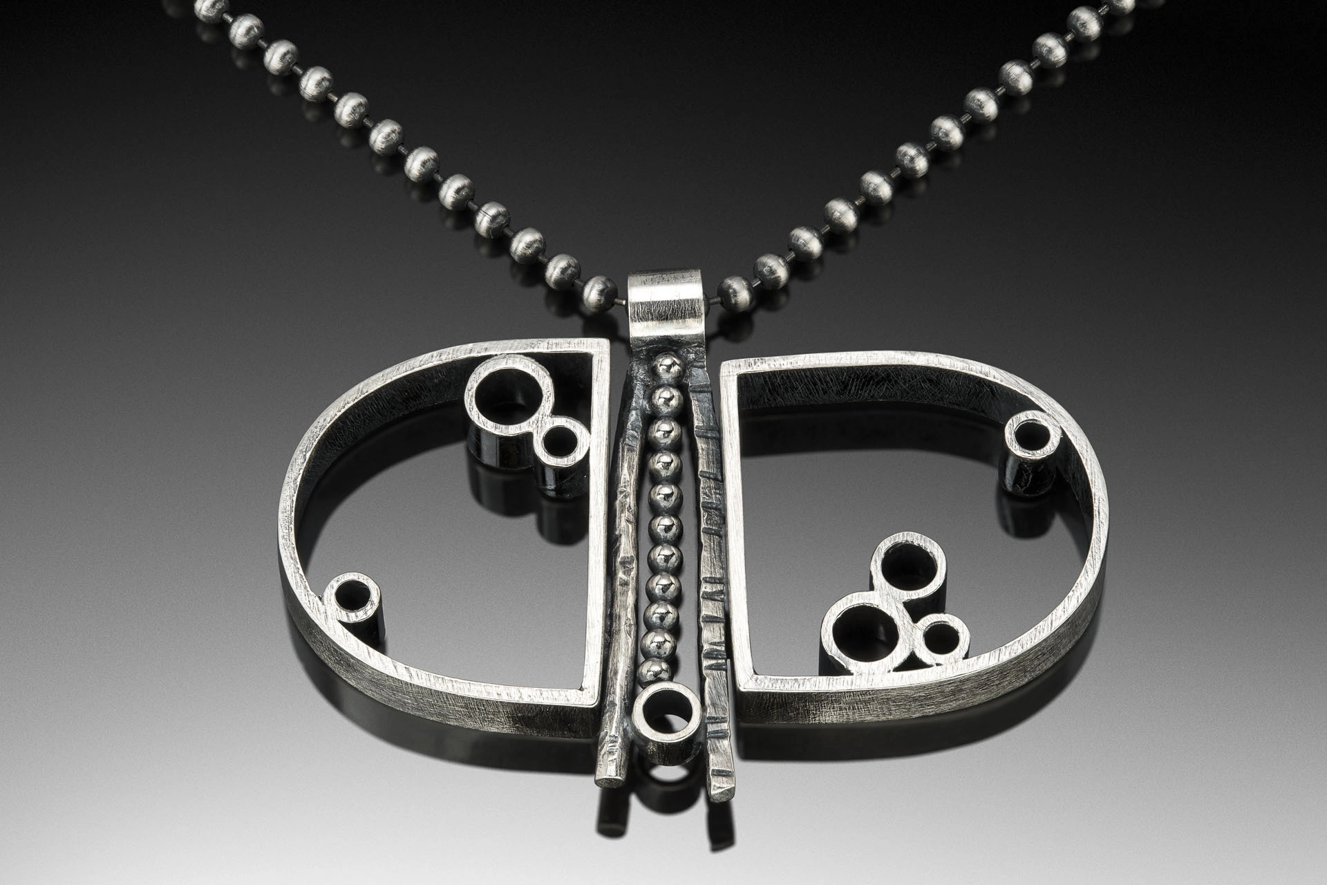 Actual geometric pendant from Jen Lawler’s festival portfolio, with paired arches, open tubes and central beads on its original photographed ground